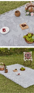 Detail of grey picnic blanket with tulip jacquard pattern and lace edges on grass