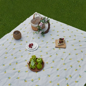 Waterproof picnic mat with yellow floral pattern and fringe edge on green grass