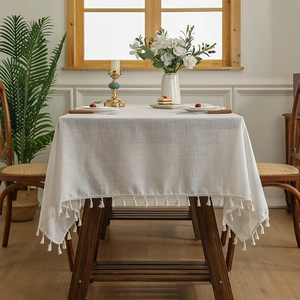 Nappe rectangulaire en lin crème avec pompons sur table en bois dans une salle à manger