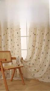Détail de rideau en lin beige avec broderies florales et bordure à pompons décoratifs