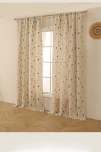 Détail du rideau en lin avec broderie florale délicate et finitions à franges blanches
