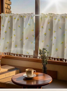 Detail of yellow floral embroidery and white tassel fringe on cotton linen cafe curtain