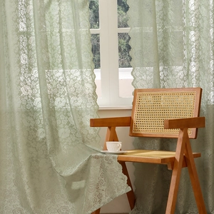 French vintage green floral lace curtain with wavy edges hanging in a cozy sunlit room