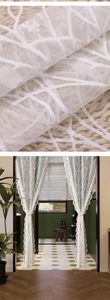 Close-up of white lace curtain fabric with delicate branch embroidery and wavy edges