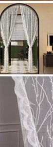 Close-up of white lace curtain with embroidered bird and branch motifs and wavy edges