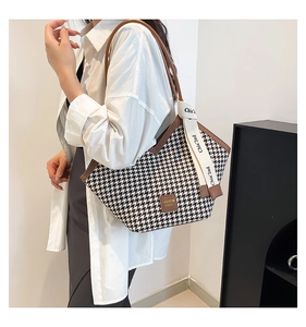 Detail of houndstooth tote bag featuring brown leather trim and fashion brand tag