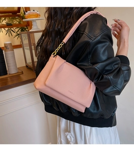Close-up of pink litchi leather bag with gold chain strap and brand logo detail