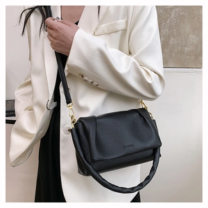 Detail of black lychee leather crossbody bag with gold hardware on a white suit