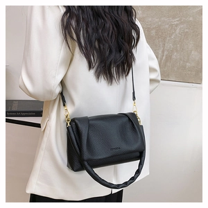 Detail of black litchi grain leather crossbody bag with gold hardware and soft handle