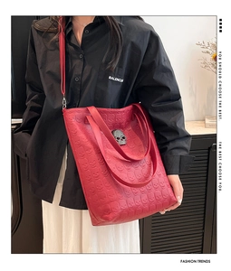 Detail of red faux leather tote bag with skull embossing and studded metallic skull charm
