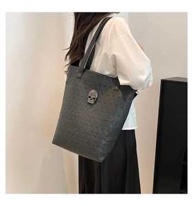Detail of black leather tote bag featuring skull embossed patterns and crystal skull charm
