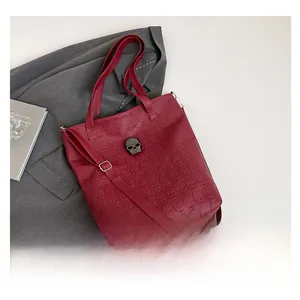 Macro view of burgundy skull embossed tote bag with studded metal skull fastener detail