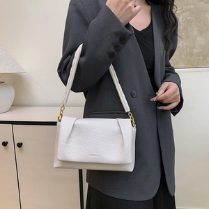 White lychee leather cloud bag with gold chain strap shown on a gray suit model