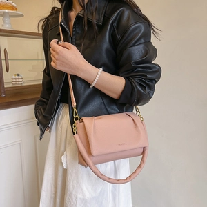 Pink pleated cloud shoulder bag with padded handle worn by a model in a cafe