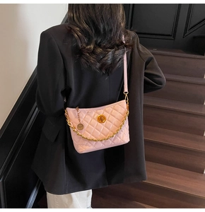 Detail of pink quilted crossbody bag with gold chain strap on model in black blazer