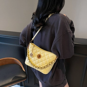 Chic yellow quilted crossbody bag with gold chain strap worn by a model in a minimalist setting