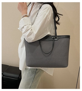 Detail of grey canvas tote bag with black leather straps worn by model on shoulder