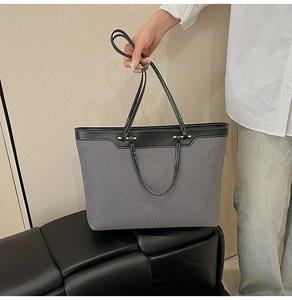 Detail view of large grey canvas tote bag with black leather straps and white contrast stitching