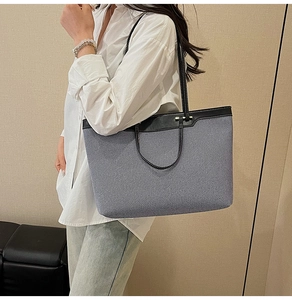 Blue denim tote bag with black leather trim worn by a model in a natural setting