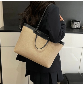 Detail of a large beige woven tote bag with black leather trim worn on the shoulder