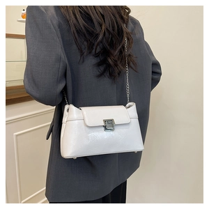 Détail d'un sac à bandoulière en cuir verni blanc avec chaîne argentée sur un blazer