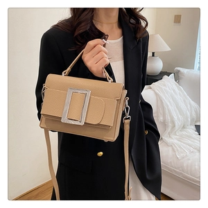 Detail of beige pebbled leather handbag with large silver buckle on a black blazer