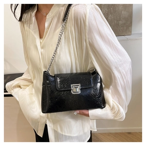 Détail d'un sac bandoulière noir à motif crocodile avec chaîne argentée et fermoir métal