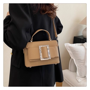 Detail of a brown textured leather shoulder bag with a silver buckle on a model