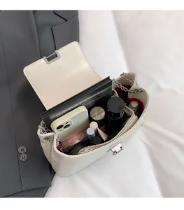 Détail de l'intérieur d'un sac crème avec bandoulière chaîne et divers cosmétiques