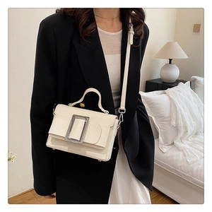 Detail of cream crossbody bag with silver buckle worn with a black blazer