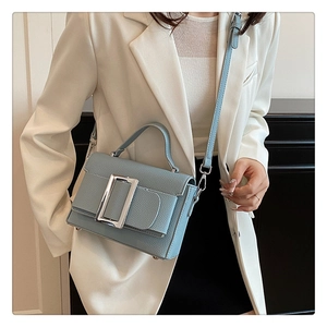 Detail of light blue lychee pattern leather bag with large silver square buckle and strap