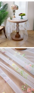 Detailed macro view of white tulle tablecloth with colorful floral embroidery on wood