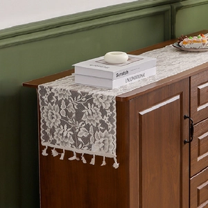 Elegant white lace table runner with floral embroidery and tassels on a wooden cabinet
