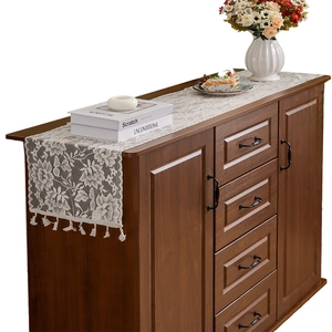 Elegant white floral lace table runner with tassels on a vintage dark wood cabinet