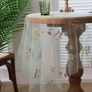 Mint green mesh tablecloth with floral and butterfly embroidery on a round wood table
