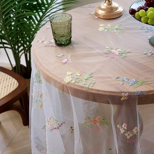 Round white mesh tablecloth with colorful floral embroidery on a wooden table