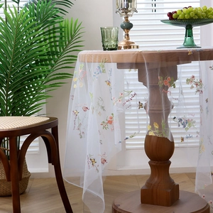 Floral embroidered sheer white tablecloth with butterfly patterns on a wooden round table