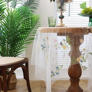 White lace tablecloth with floral and butterfly embroidery on a round wooden table