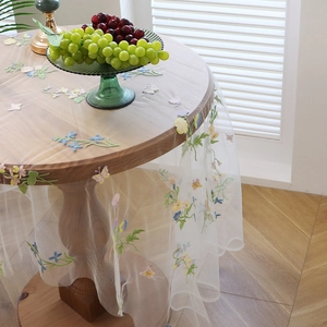 Transparent lace tablecloth with floral butterfly embroidery and wavy edges on a round table