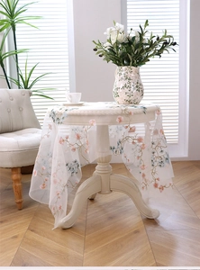 Detail of white mesh tablecloth with pink floral and pine embroidery on a wooden table