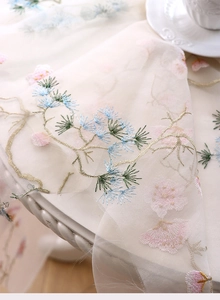 Macro shot of high-quality floral embroidery and pine needle patterns on white tulle fabric