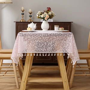 Pink floral lace tablecloth with white tassel edges on a light wood dining table