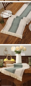 Close-up of beige and green striped table runner with woven texture and fringe