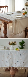 Detailed embroidery of yellow daisies and bees on a linen tablecloth with tassels