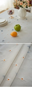 Close-up of linen tablecloth featuring daisy and bee embroidery with detailed fabric texture
