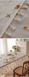 Close-up of floral embroidery and delicate lace fringe on a beige cotton tablecloth