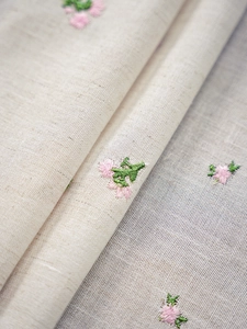 Close-up of premium linen fabric featuring elegant pink floral embroidery and green leaves