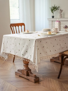 Close-up of cream linen tablecloth with floral embroidery and beige tassel fringe edge