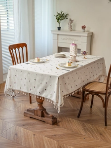 Detail of pink floral embroidery and cotton tassels on a beige linen tablecloth