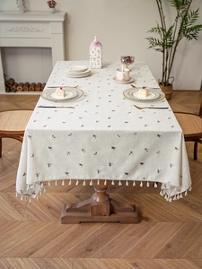Detail showing pastoral cream linen tablecloth with floral embroidery and white fringe edges